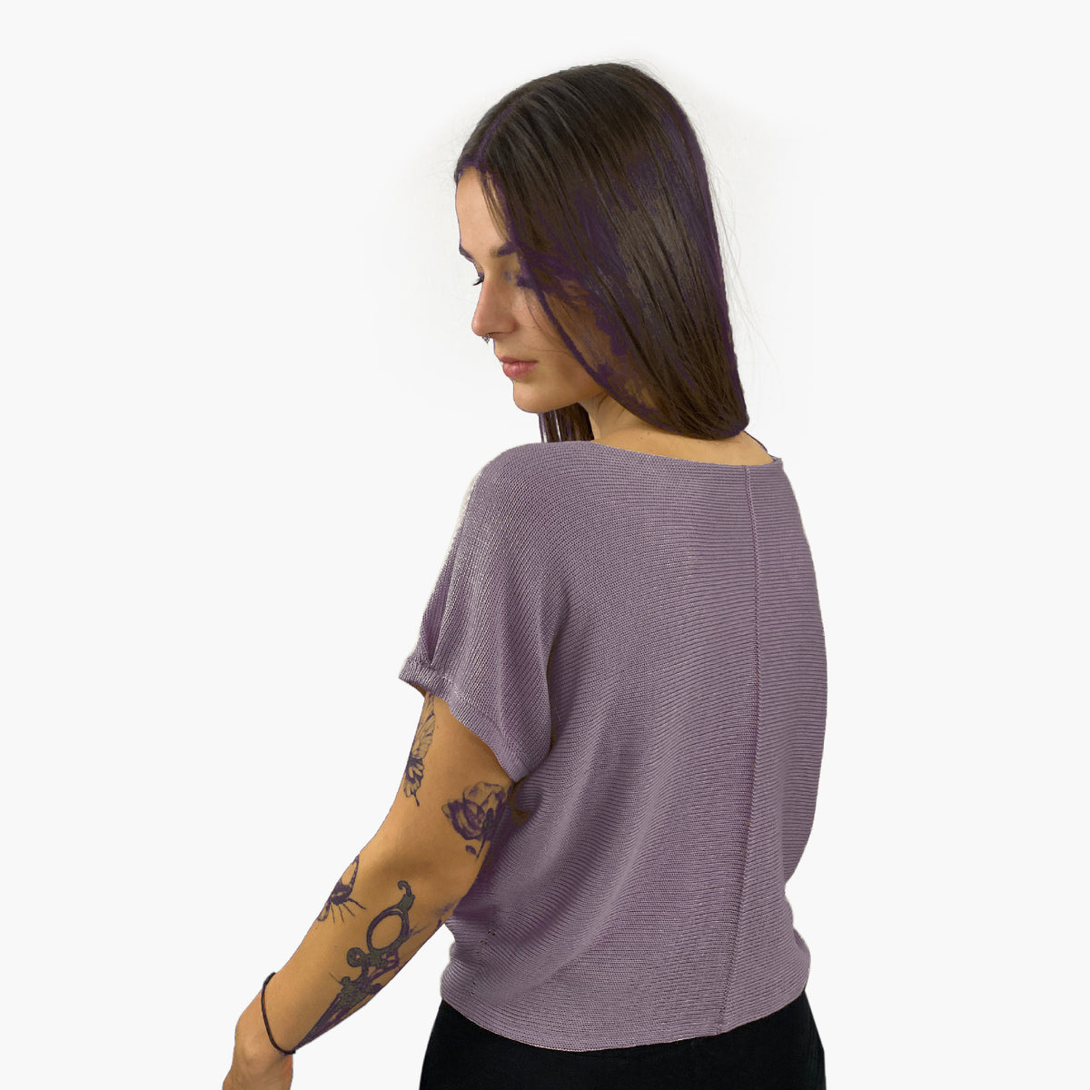 Unser Model mit glatten, Langem, braunem Haar und Taatoos (Schmetterling, Scorpion) auf dem Arm trägt ein seidig gänzendes T-shirt von vincente. Das Shirt ist aus Tencel/Lyocell gestrickt hat eine kleine Falte an dem kurzen Arm und ist Flieder-Grau. Hier ist es von hinten zu sehen, so daß man die Naht sieht, mit der das Shirt zusammengehäkelt wurde.
