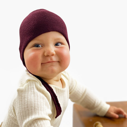 Pausbäckiges Baby lacht in die Kamera. Es trägt eine gestrickte Haube von vincente. Mit verstellbarem Bändchen zum zuknöpfen und kleinem beigen Knopf.