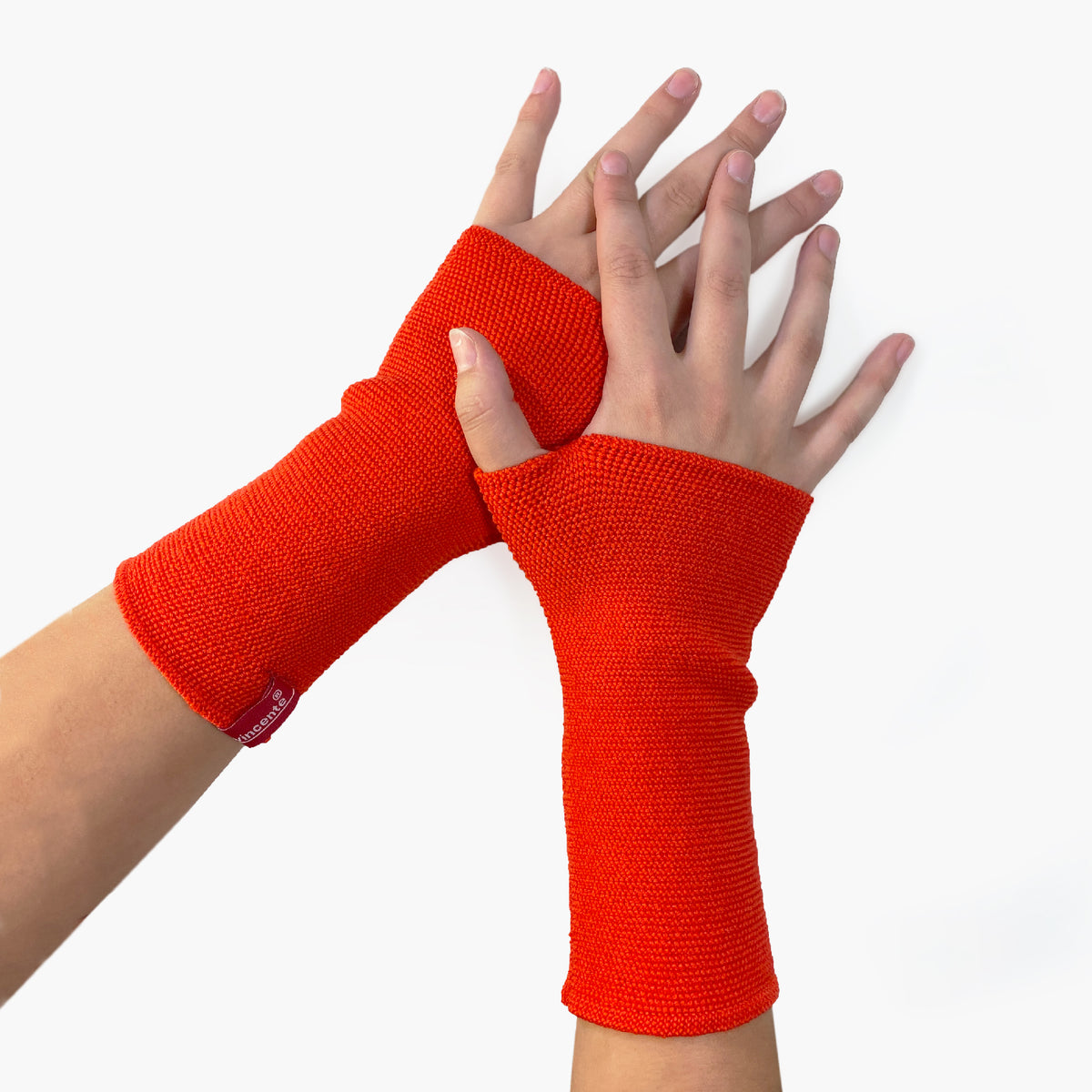 zwei Hände tragen Orangerote Armstulpen mit abgenähtem Daumenloch. Man sieht das außenliegende Knötchenmuster. Innen sind die Stulpen Glatt rechts gestrickt.