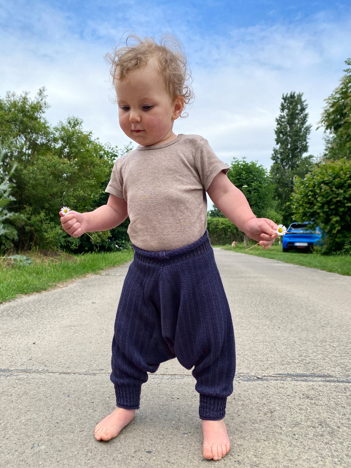 tanzendes Baby mit einem Gänseblümchen in der Hand. Es trägt eine Sarouelhose von vincente aus Tencel/Lyocell gestrickt in Dunkelblau