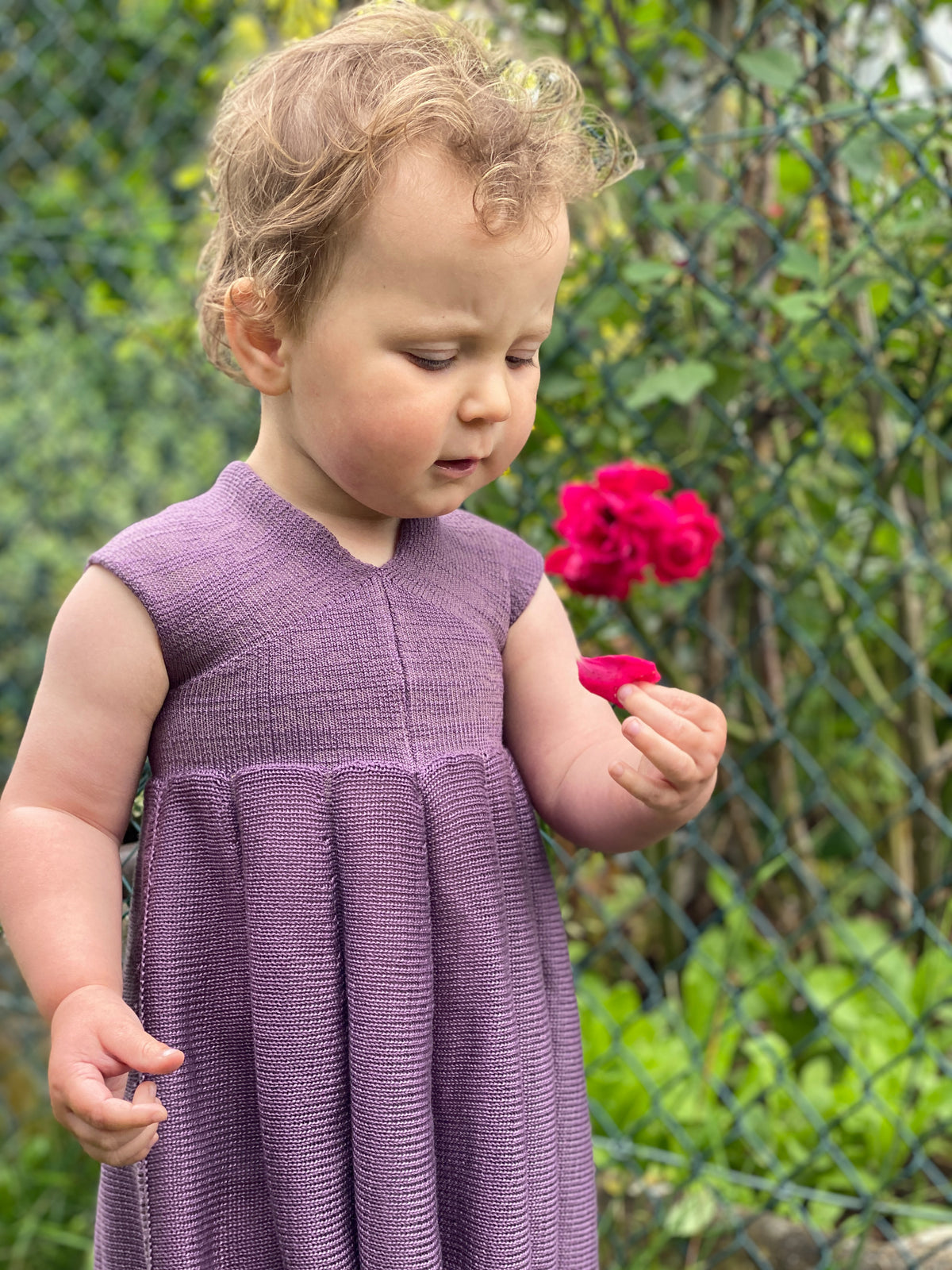 Ein Mädchen mit einer roten Rose in der Hand trägt ein Sommerkleid von vincente aus Tencel/Lyocell gestrickt in Lila