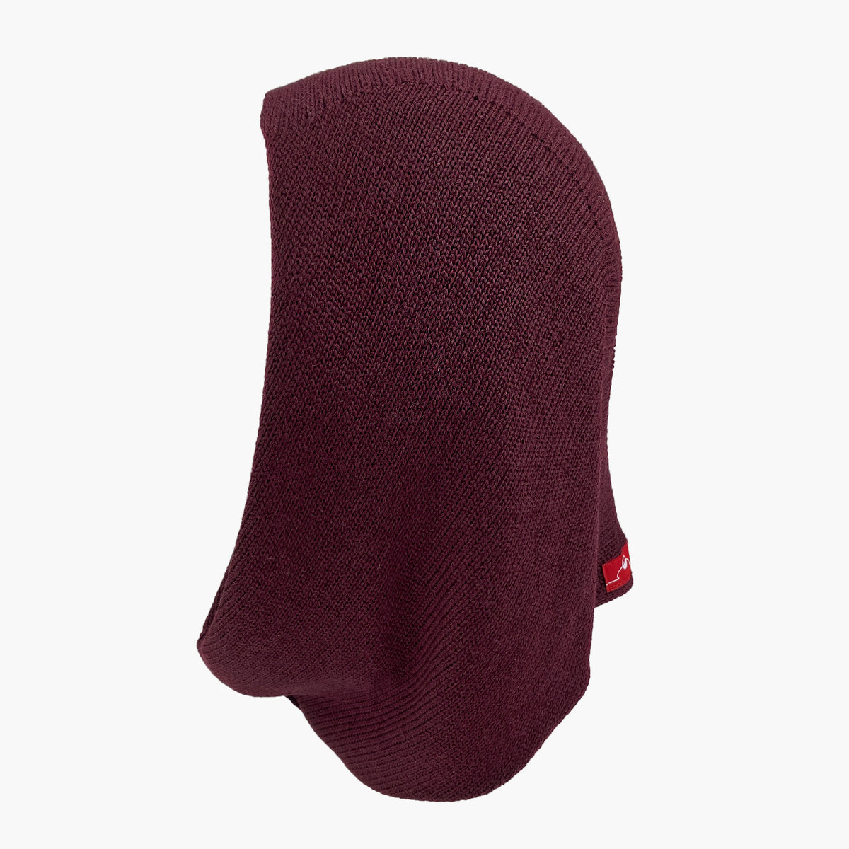 Mütze deren Form den Kopf umspielt, und auch das Kinn bedeckt, ähnlich einer geschlossenen Kapuze. Die Balaclava liegt  flach, so daß man diese Kapuzenform: oben breiter zum Hals Schmal zulaufend, gut sehen kann. Sie ist Bordeauxrot und aus Merinowolle gestrickt.