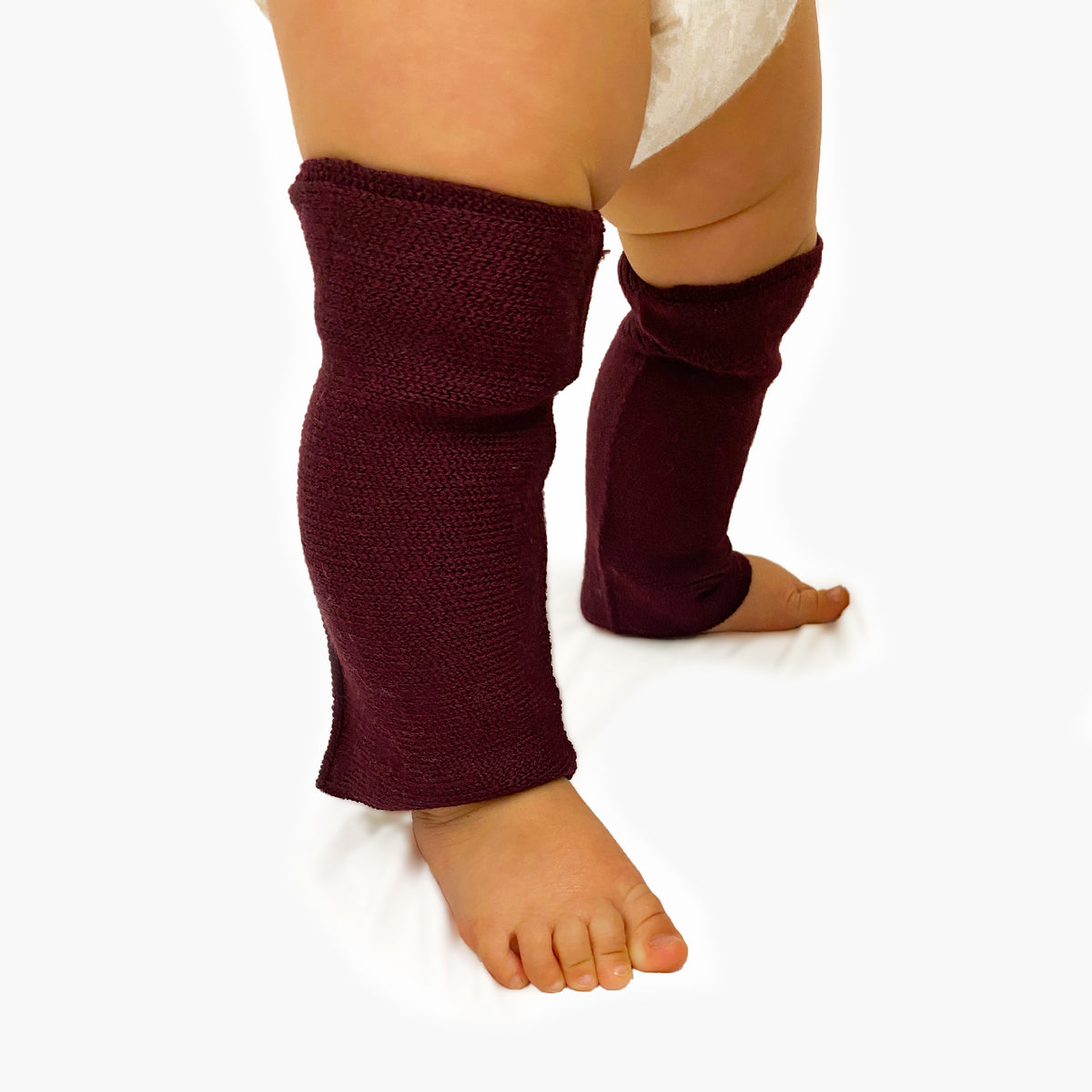 Man sieht speckige Babybeine angezogen mit Beinstulpen aus Wolle gestrickt in Bordeauxrot