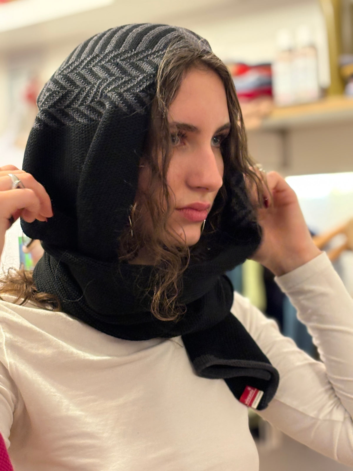 gestrickter Kapuzenschal von vincente aus Merinowolle mit Fischgrätmuster. Der Schal wird von einer jungen Frau getragen, die im Berliner Designatelier steht