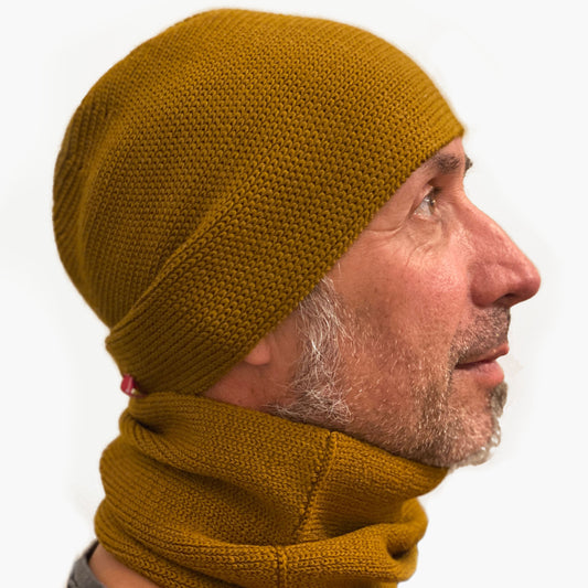 Ein Mann trägt eine Broncefarbene Wollmütze aus Merinowolle quer in Kopf-Form gestrickt. Das Fangpatentmuster bedeutet, daß Innen ein Knötchenmuster und außen ein klassiches Rechte Maschenmuster zu sehen ist. Wenn man den Beanie umkrempelt und als Dockermütze trägt ist jeweils das andere Muster zu sehen. Das rote vincente-Label mit der kleinen Ente ist am Rand angenäht. Die Mütze kann insideout getragen werden.