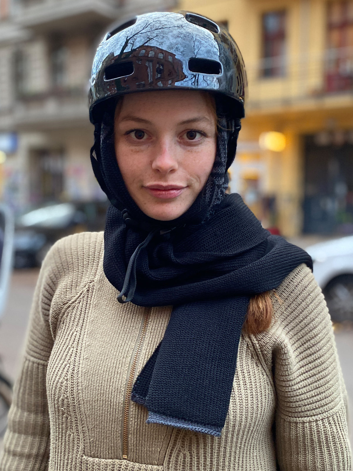 Schal mit eingearbeiteter Kapuze im Fischgraetmusterschwarz/Grau. Das Mdell trägt einen Fahrradhelm üer dem Kapuzenschal