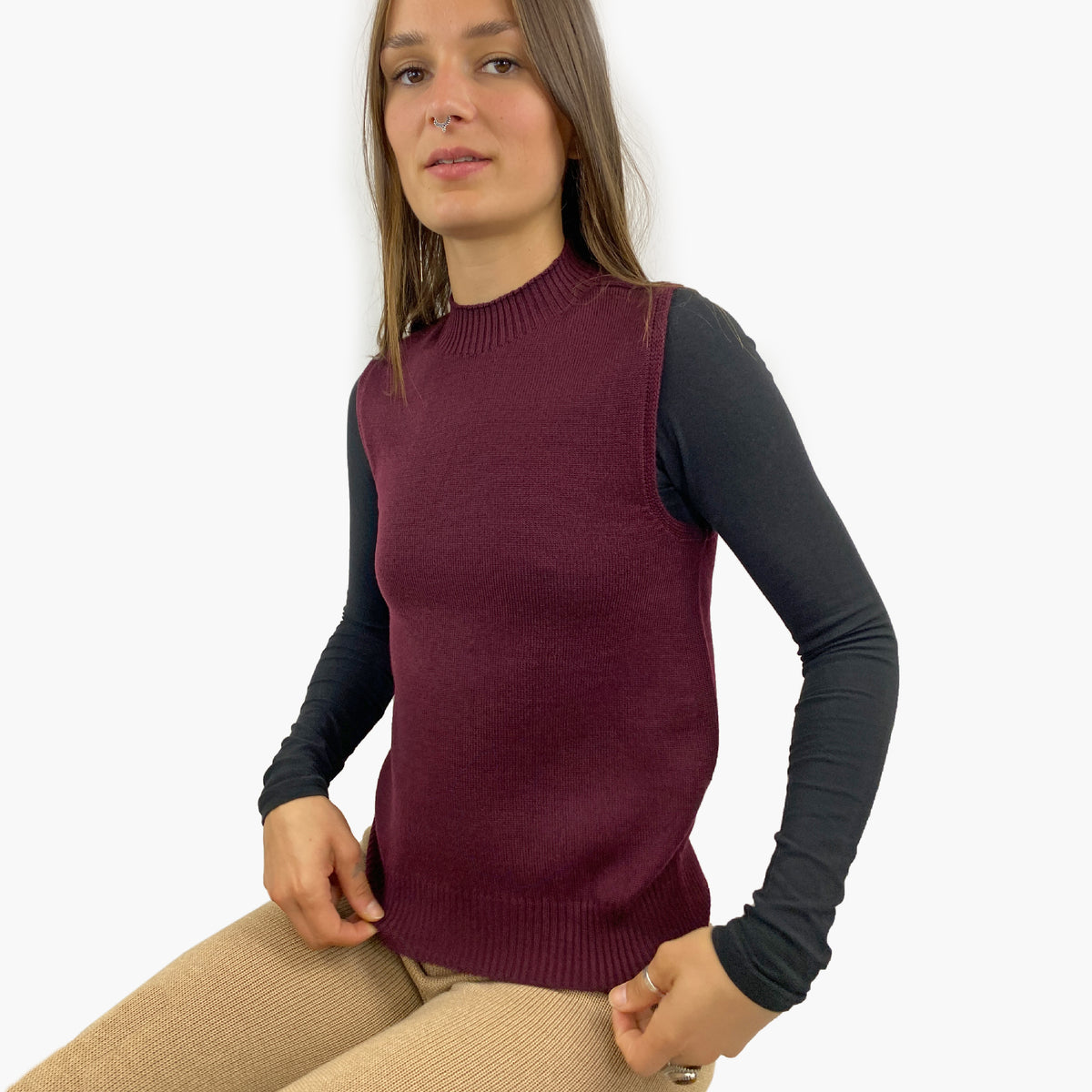 eine junge Fraumit langen Haaren trägt einen glatt gestrickten, Bordeauxfarben Pullunder mit hochgeschnittenem Rundhalsauschnitt im rechts/links Muster. Auch der untere Abschluß ist im rechts/links Muster.