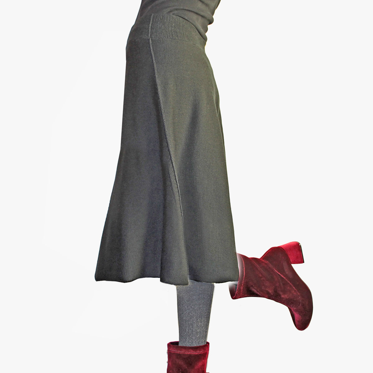 Man sieht ein Model in einem ausgestellten über-knielangen Designer-Strickrock in Grau. Handgefertigt im Modeatelier vincente Sie trägt samtrote Schuhe mit hohen Absätzen.