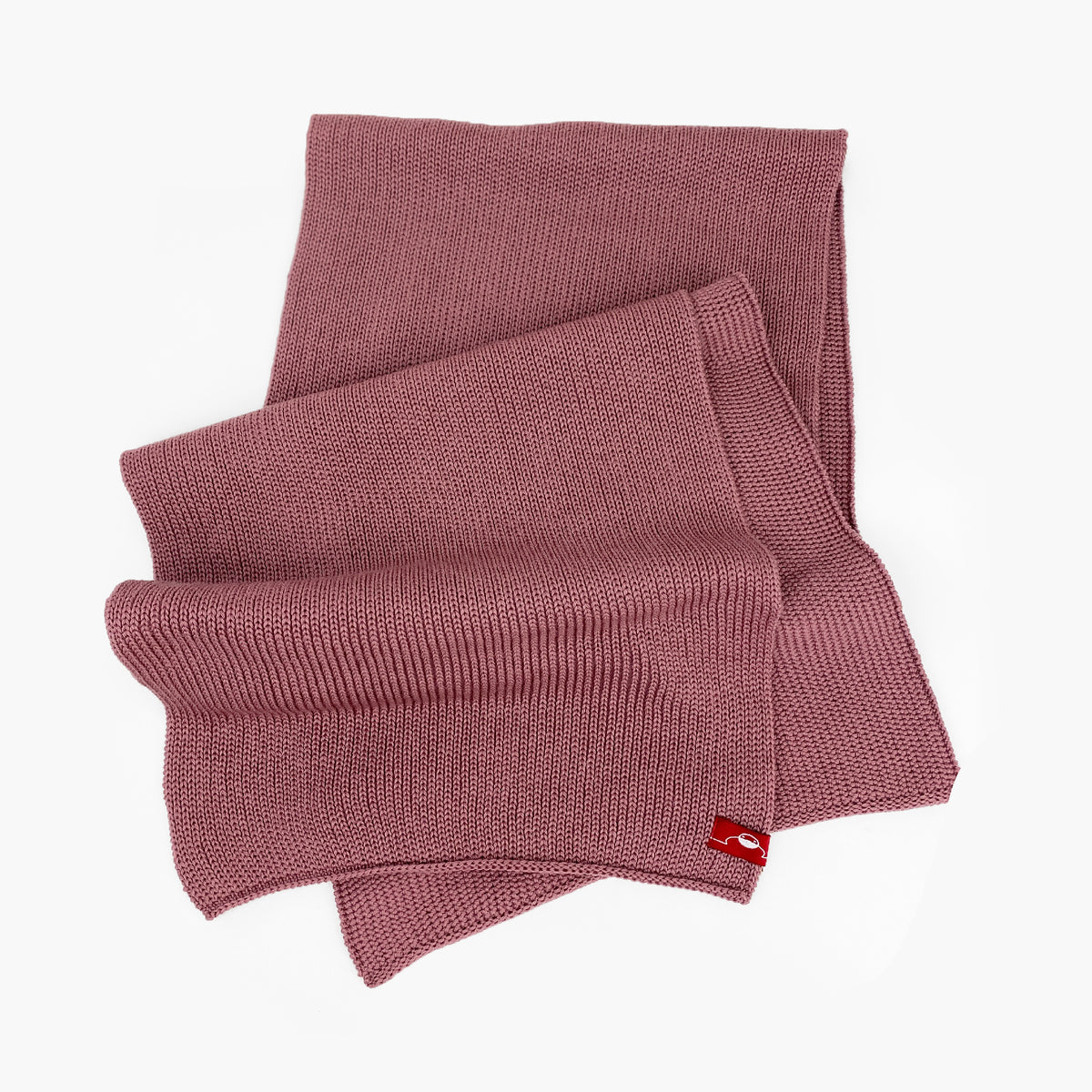 Rosenholz farbener, gestrickter Schal im Fangpatentmuster. Eine Seite sieht glatt rechts gestrickt, die andere Seite sieht aus wie minikleine Muscheln oder Punkte. Der Wollschal ist zu einem Haufen drapiert, so sieht man den weichen Fall.