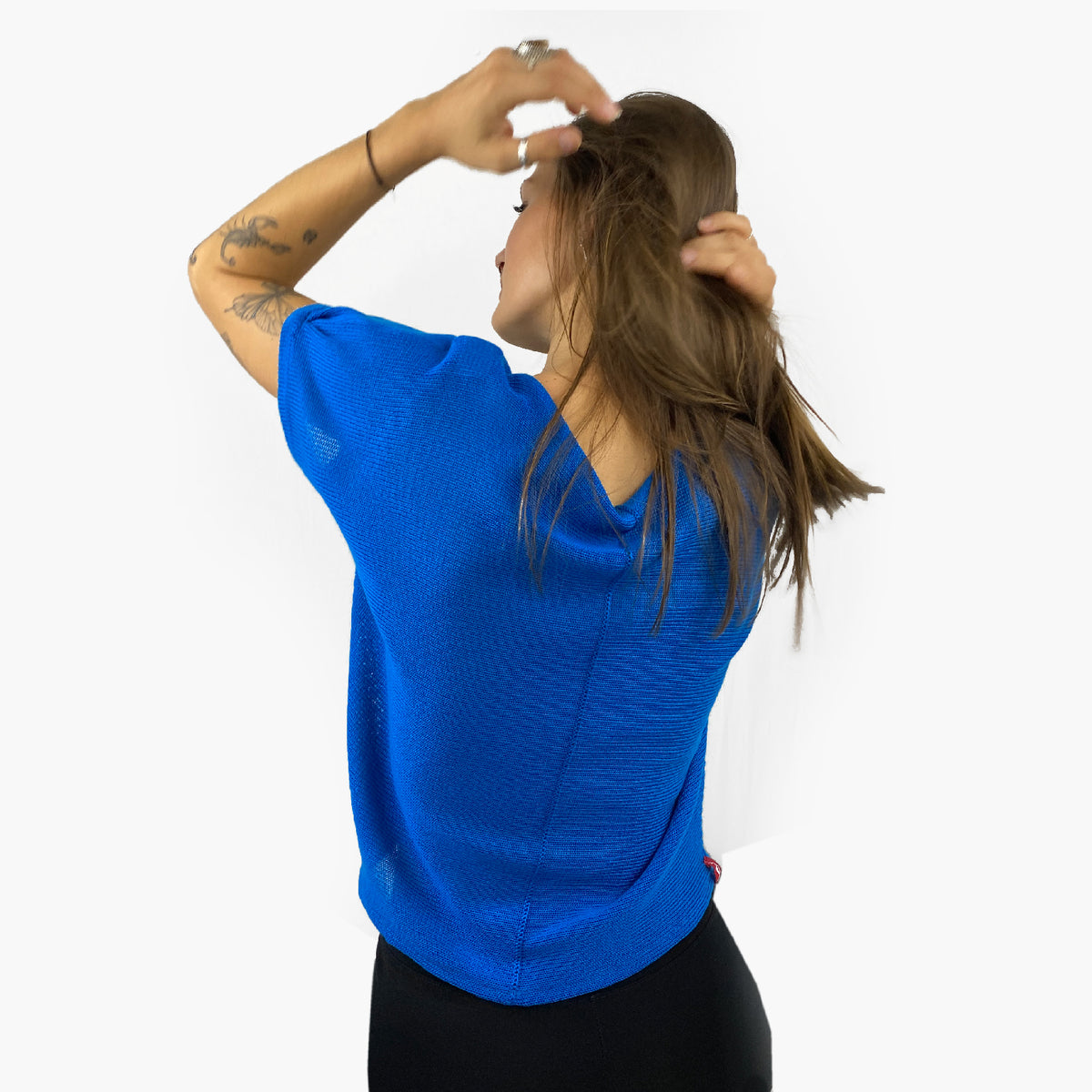 Unser Model mit glatten, Langem, braunem Haar und Taatoos (Schmetterling, Scorpion) auf dem Arm trägt ein seidig gänzendes T-shirt von vincente. Das Shirt ist aus Tencel/Lyocell gestrickt hat eine kleine Falte an dem kurzen Arm und ist leuchtend Blau. Hier ist es von hinten zu sehen, so daß man die Naht sieht, mit der das Shirt zusammengehäkelt wurde.