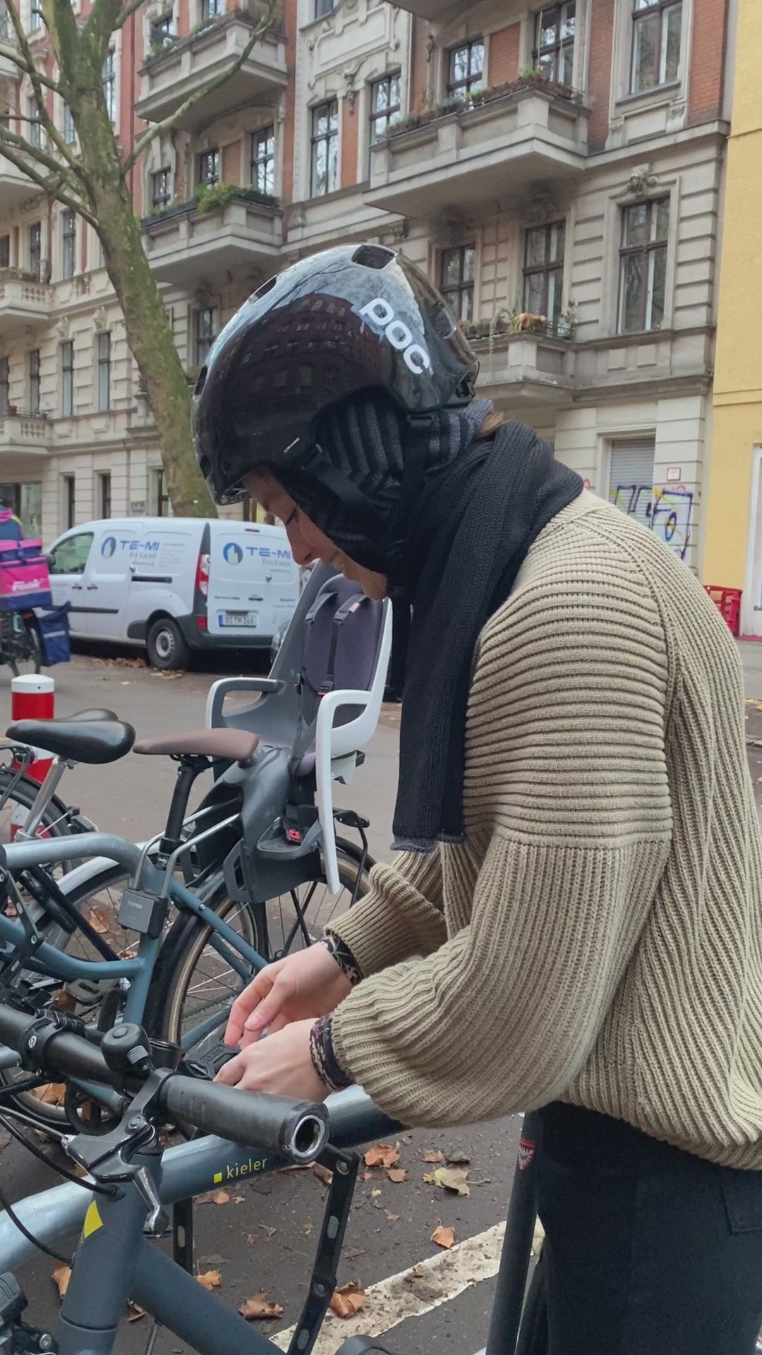 Film in dem eine junge Frau den Schal mit eingearbeiteter Kapuze im Fischgraetmuster unter ihrem Fahrradhelm trägt. Der Schal ist Grau und Schwarz.