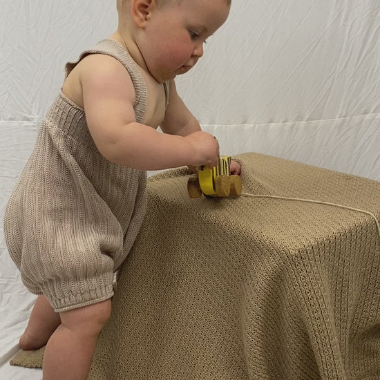 Kurzer Film in dem ein kleines Baby eine Kurze gestrickte Hose mit Hosenträgern trägt. Das Baby versucht dauernd sich hinzustellen und gleichzeitig an seiner Holzente zu saugen.