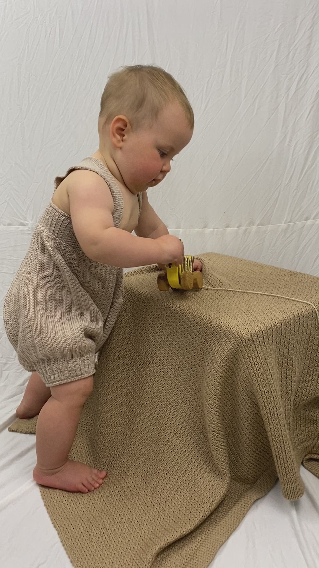 Kurzer Film in dem ein kleines Baby eine Kurze gestrickte Hose mit Hosenträgern trägt. Das Baby versucht dauernd sich hinzustellen und gleichzeitig an seiner Holzente zu saugen.