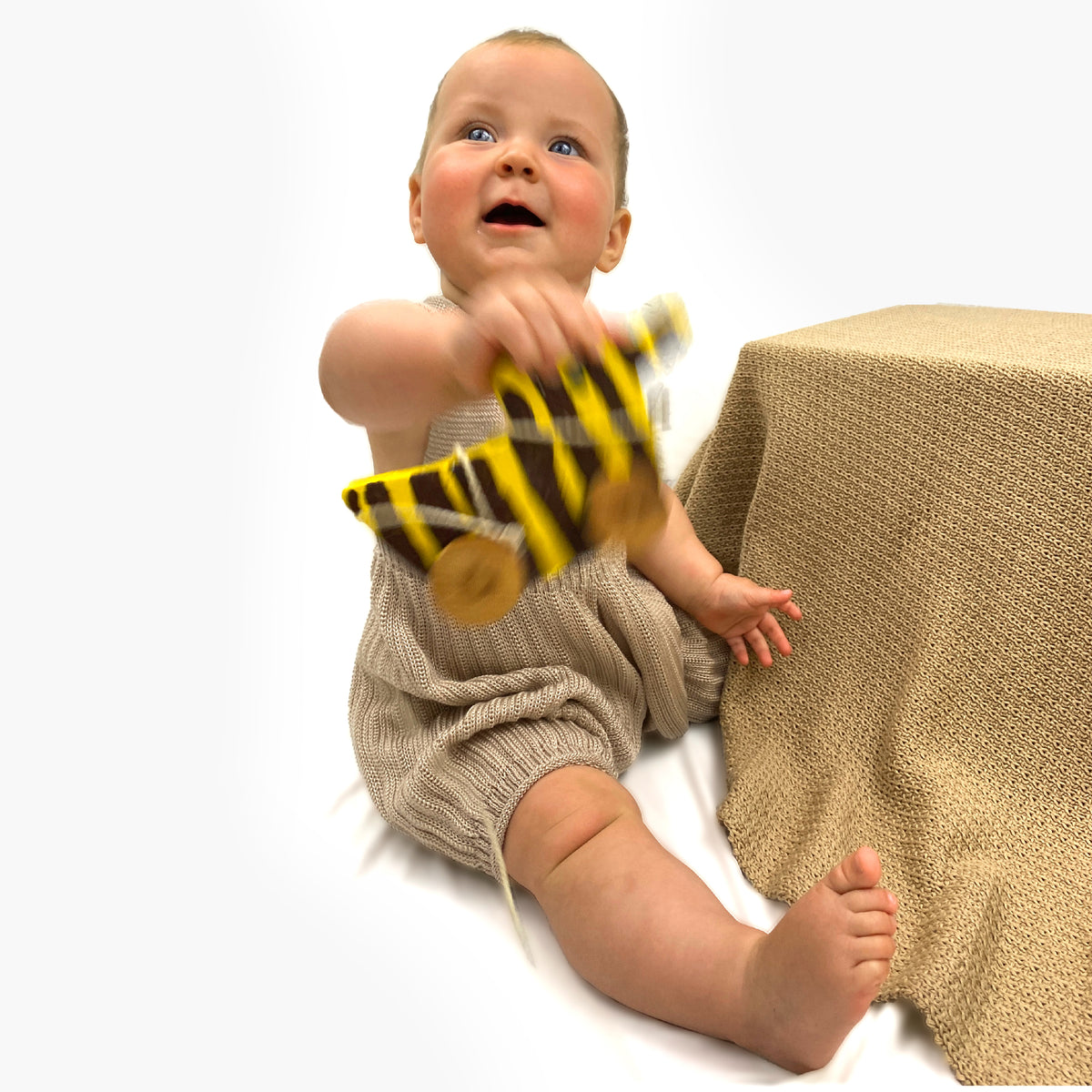 Ein Baby mit einer Tigerente aus Holz in der Hand trägt eine gestrickte kurze Sommerhose aus Tencel/Lyocell mit tiefen Schritt und viel Platz für Windeln. Die Hose von vincente hat hochelastische Hosenträger  und ist Beige/Champagnerfarben