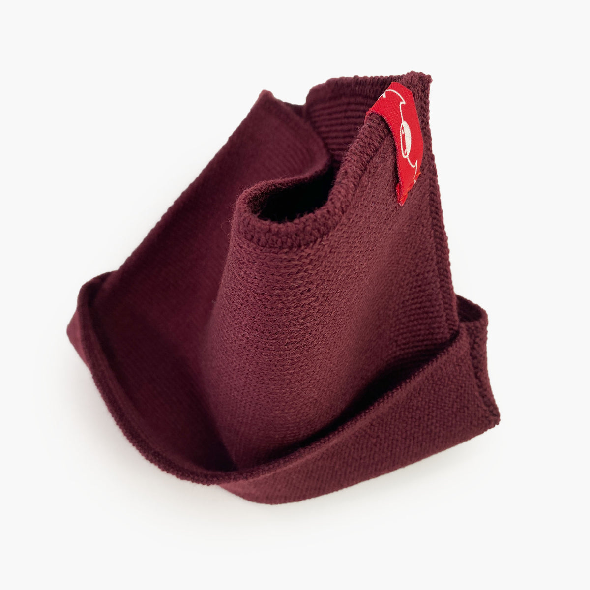 Bordeaux farbener gestrickter Loop außen glatt rechts gestrick. An einer Stelle ist der Schlauch umgeschlagen so sieht man das Innere feine Knötchen-Muster. das Rote/Weiße vincente-Label ist angenäht.