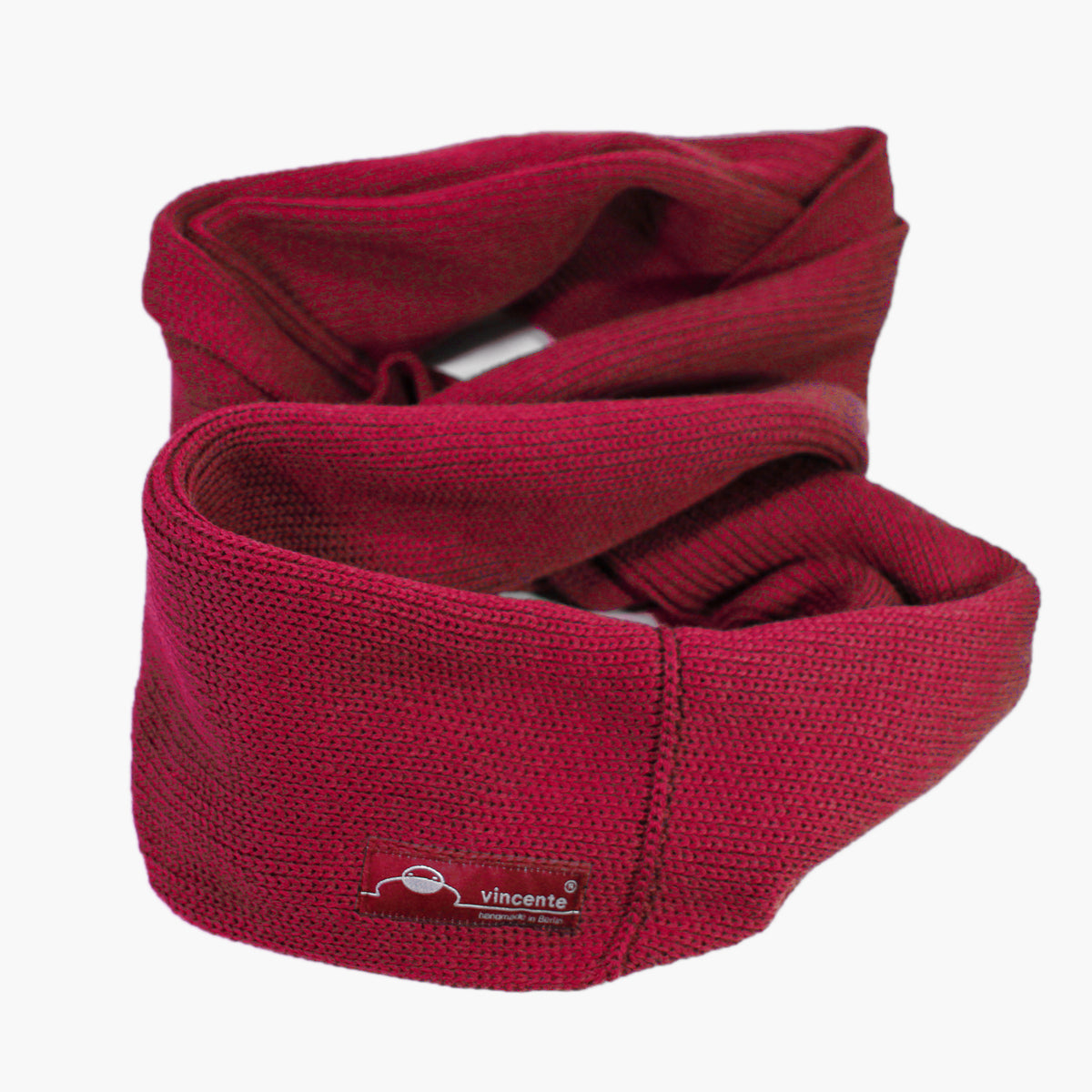 Roter, gestrickter Loop im Fangpatentmuster. Eine Seite sieht glatt rechts gestrickt, die andere Seite hat ein feines Muschelmuster. Der Schal ist zu einem Haufen drapiert ist, so sieht man den weichen Fall des Wollschals sieht.