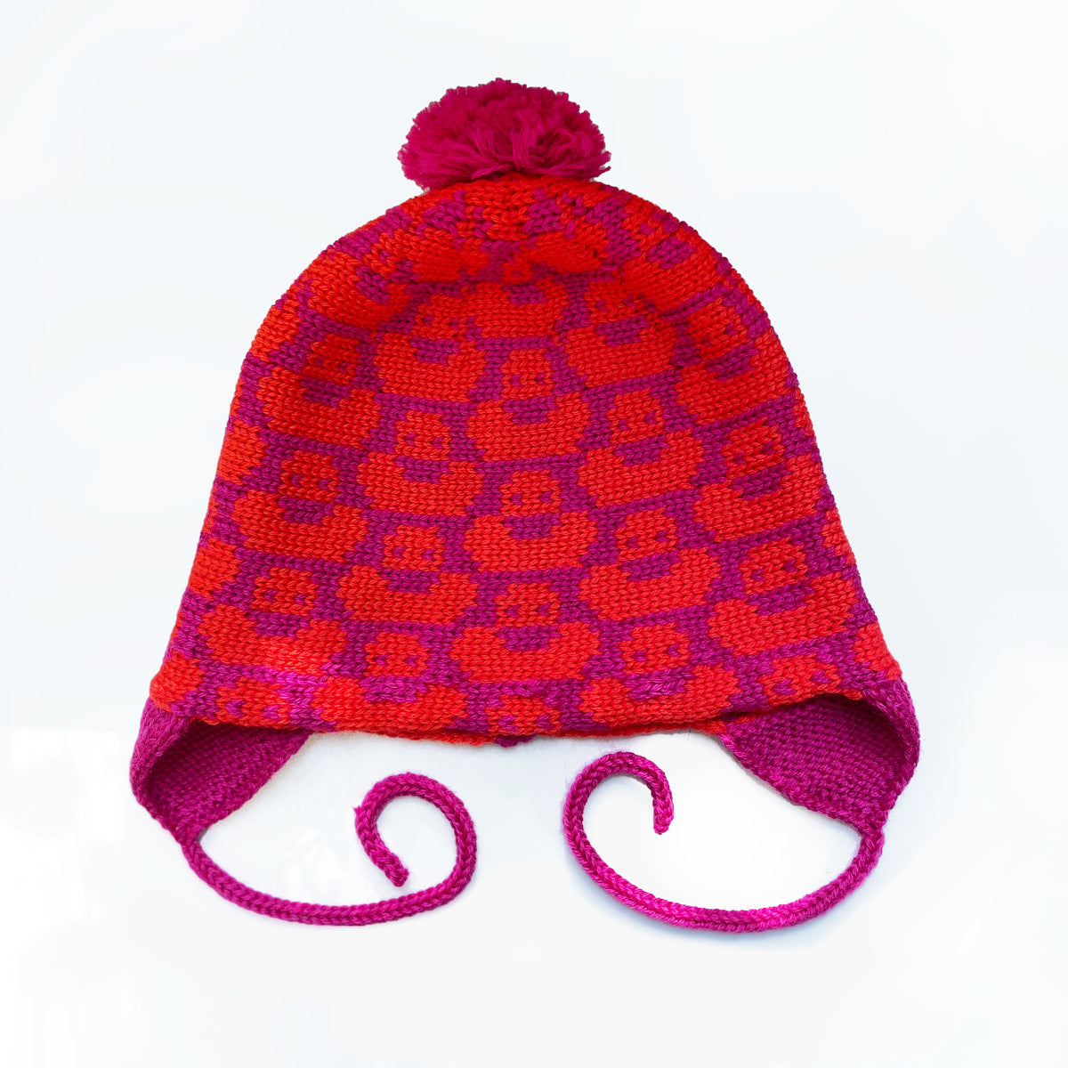 Pink/Orangerote Mütze für Babies und Kinder mit einem fortlaufenden Muster mit kleinen Enten. Die Babymütze hat eine Bommel und angestrickte Ohrläppchen mit Bändern zum festbinden. Sie ist aufwendig der Kopfform nachgestrickt und paßt sich sehr gut an. Das rote Label mit der kleinen Ente ist hinten angenäht.