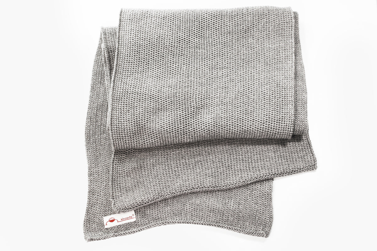 Silbergrauer gestrickter Schal im Fangpatentmuster. Eine Seite sieht glatt rechts gestrickt, die andere Seite sieht aus wie minikleine Muscheln oder Punkte. Der Wollschal ist zu einem Haufen drapiert, so sieht man den weichen Fall