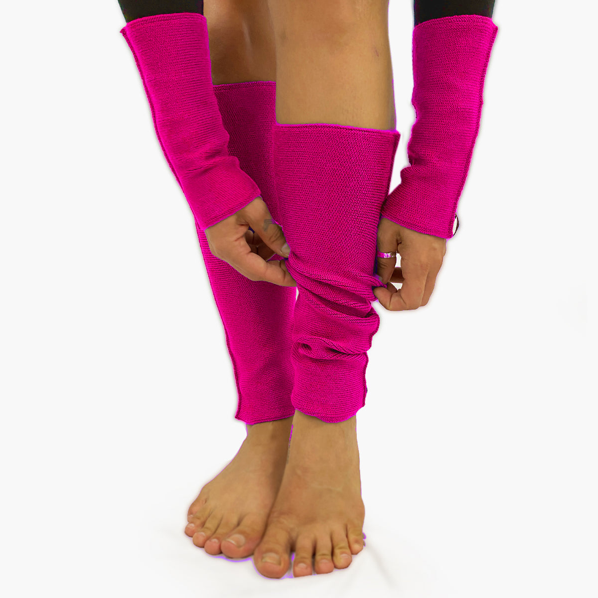eine Frau mit nackten Füßen schopped Ihre pinken Beinstulpen zurecht .Man sieht das außenliegende Glatt Rechts Muster. An den Handgelenken trägt Sie Armstulpen in der gleichen Qualität und Farbe. Innen sind die Stulpen in einem Feinen Knötchenmuster gestrickt, man kann sie auch Innsideout tragen