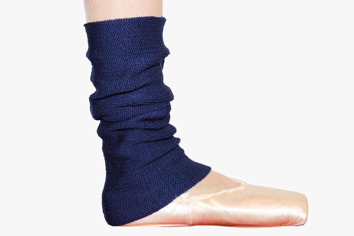 Man sieht ein Täzer*innnen- Bein mit rosafarbenen Ballet Spitzenschuhen. Um die Knöchel trägt es eine Royalblaue gestrickte Wollstulpe von vincente, die dicht zusammen geschoppt ist.