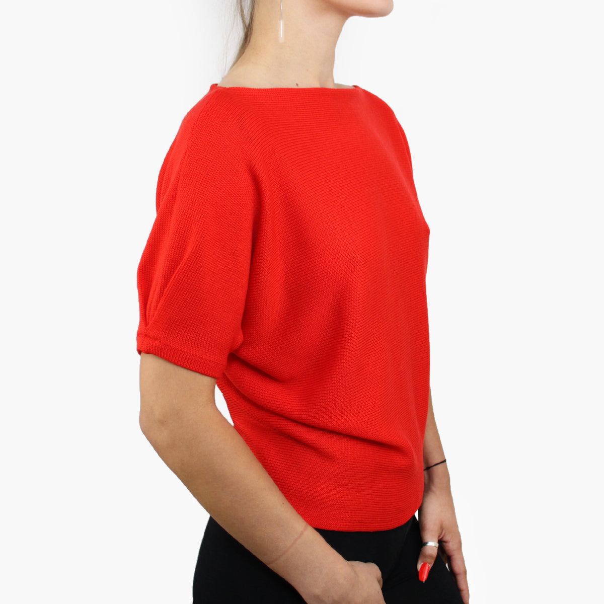 Man sieht den Rupf eines Models. Es trägt einen Orangeroten quer gestrickterPullover mit kurzen, angeschnittenen Ärmeln ähnlich wie beim T-Shirt. Mit kleiner Falte am Armende.
