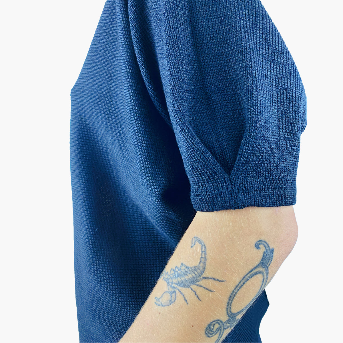 Großansicht der Ärmelfalte des quer gestrickten Pullovers. Der Pulli ist Blau und  man sieht noch ein bischen des Unterarms des Model auf dem ein Scorpion tättowiert ist.