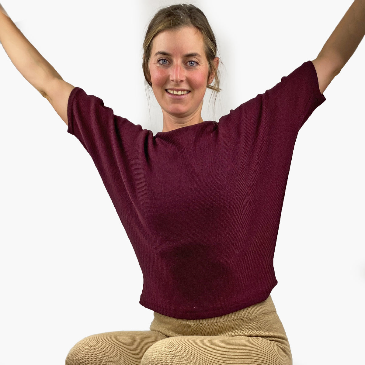 Ein Model trägt einen quer gestrickten , bordeauxfarbenen Pullover mit kurzen, angeschnittenen Ärmeln ähnlich wie beim T-Shirt. Mit kleiner Falte am Armende. 
