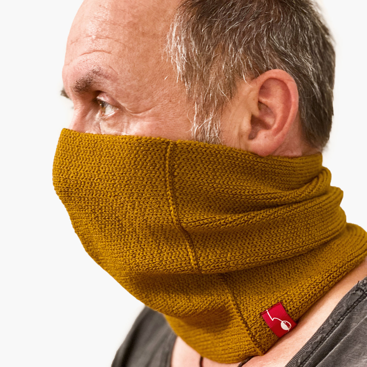 Ein Mann trägt einen Bronce  farbenen gestrickten Loop außen glatt rechts gestrick. Er hat den Loop bis über die Nase gezogen.