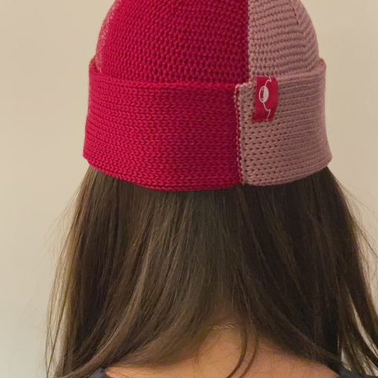 Eine Frau dreht sich im Kreis so sieht man den Farbverlauf der Beanie-Mütze, der sich wie in verschiedenen Rot und Rosa Kobinationen ändert.