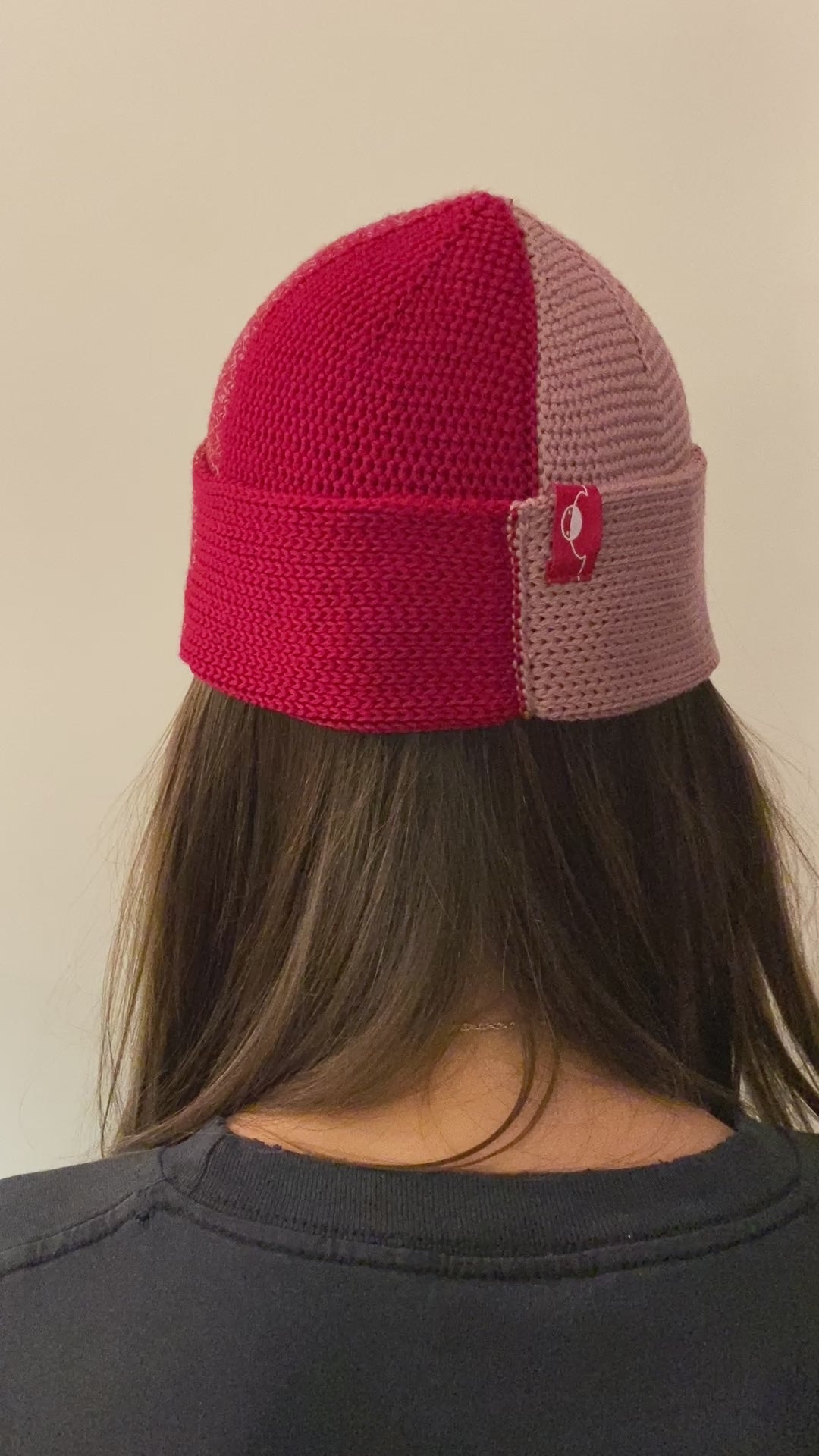 Eine Frau dreht sich im Kreis so sieht man den Farbverlauf der Beanie-Mütze, der sich wie in verschiedenen Rot und Rosa Kobinationen ändert.