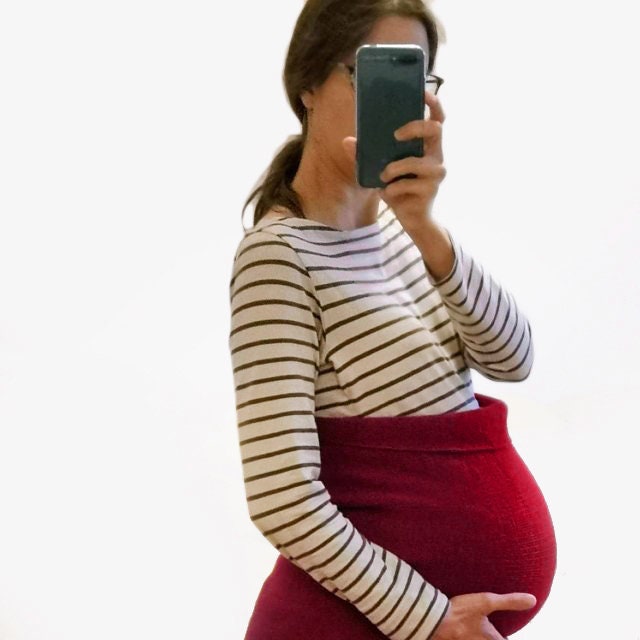 eine Frau macht von sich ein Selfi, sie trägt über Ihren Babybauch einen Rot