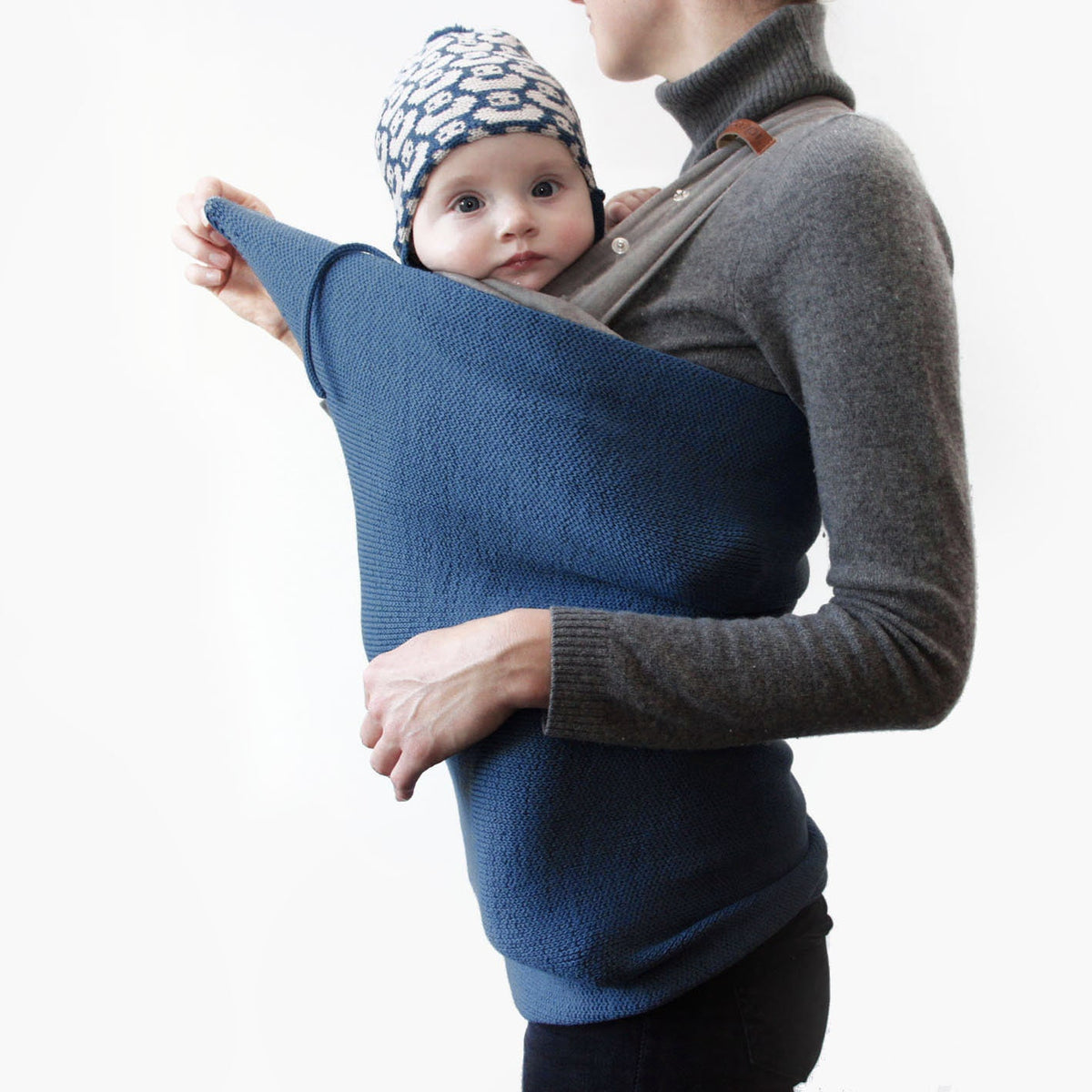 Du siehst ein Baby in einer Trage auf Mama´s Bauch gebunden. Es trägt eine Entenmütze von vincente. Über das Baby und die Mutter ist ein Strickschlauch gezogen, der das Baby vom Hals an abwärts verdeckt und auch den Po der Mutter nahezu umschließt. Man sieht, daß der Schlauch sehr elastisch ist und sich allen Formen eng anpaßt.