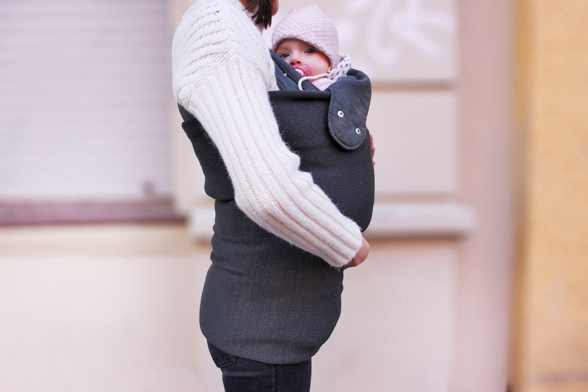 Du siehst ein Baby in einer Trage auf Mama´s Bauch gebunden. Es trägt eine Entenmütze von vincente. Über das Baby und die Mutter ist ein Strickschlauch gezogen, der das Baby vom Hals an abwärts verdeckt und auch den Po der Mutter nahezu umschließt. Man sieht, daß der Schlauch sehr elastisch ist und sich allen Formen eng anpaßt.