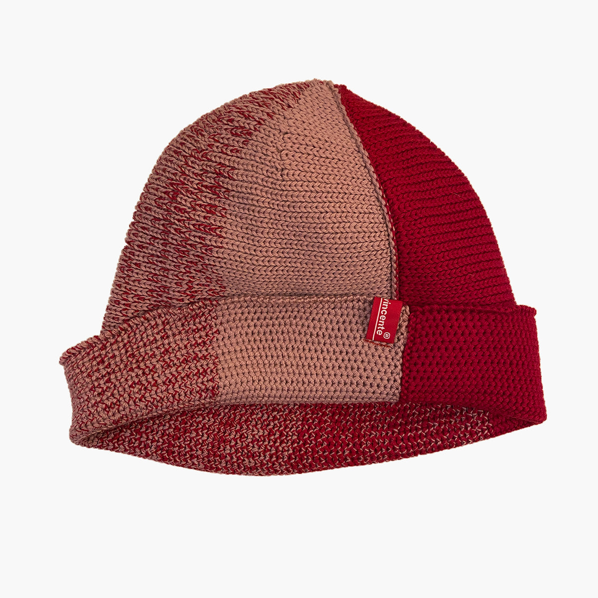 Rot/Rosenholz farbene Beanie. Der Rand ist umgeschlagen, wie bei einer Dockermütze. So sieht man das Innere  Knötchenmuster, wärend die Mütze außen rechtsgestrickt erscheint. Die Mütze hat einen Farbverlauf, der sich im Kreis wie Tortenstücke verhält. Ein Stück ist Rosenholz-farben ein Stück Rot. Dazwischen  michen sich die beiden Farben im Farbverlauf von Rosa mit etwas Rot dann etwas mehr Rot usw.
