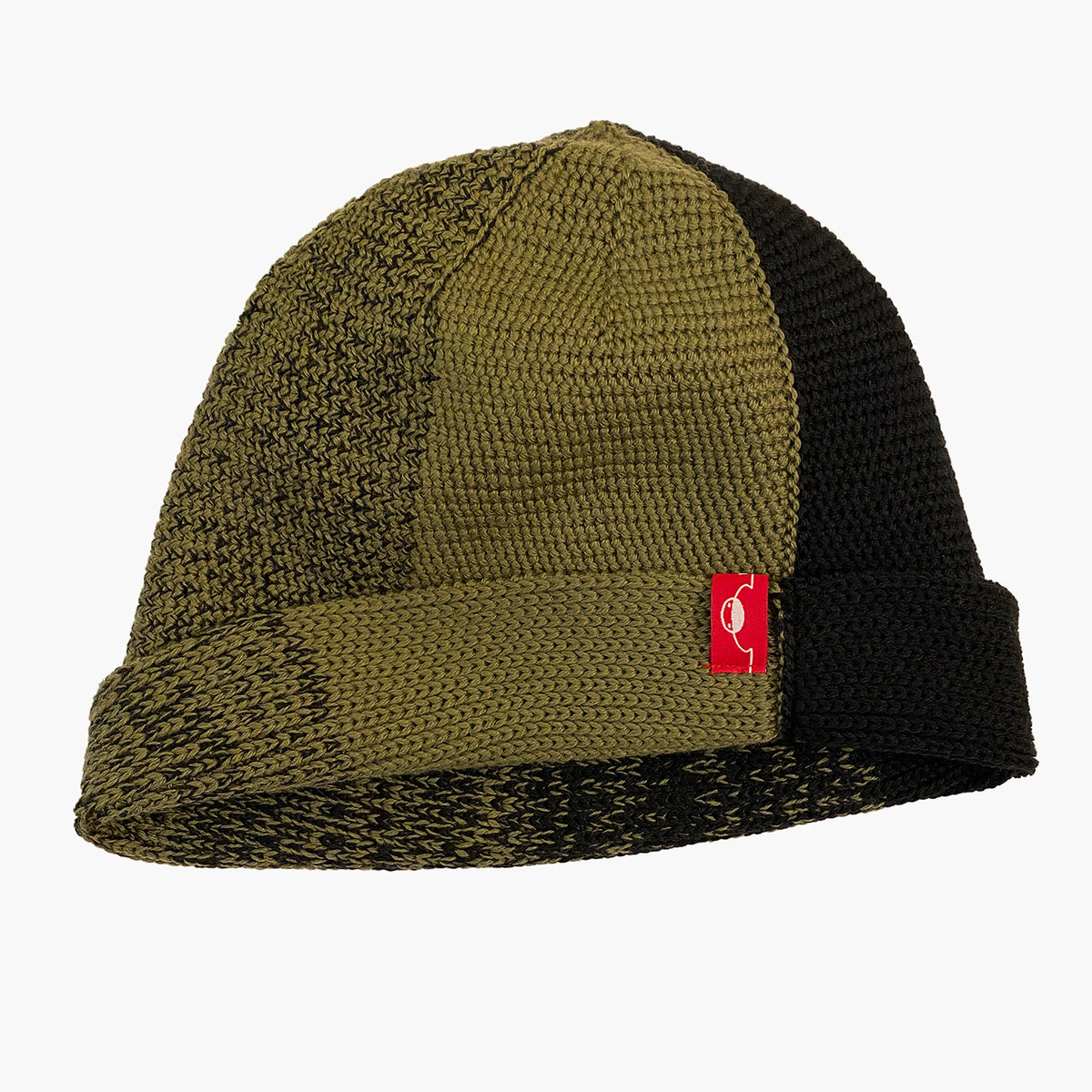 Olive/Schwarze  Beanie. Der Rand ist umgeschlagen, wie bei einer Dockermütze.  Die Mütze hat einen Farbverlauf, der sich im Kreis wie Tortenstücke verhält. Ein Stück ist Olive-farben ein Stück Schwarz. Dazwischen  michen sich die beiden Farben im Farbverlauf von Olive mit etwas Schwarz dann etwas mehr Schwarz usw.