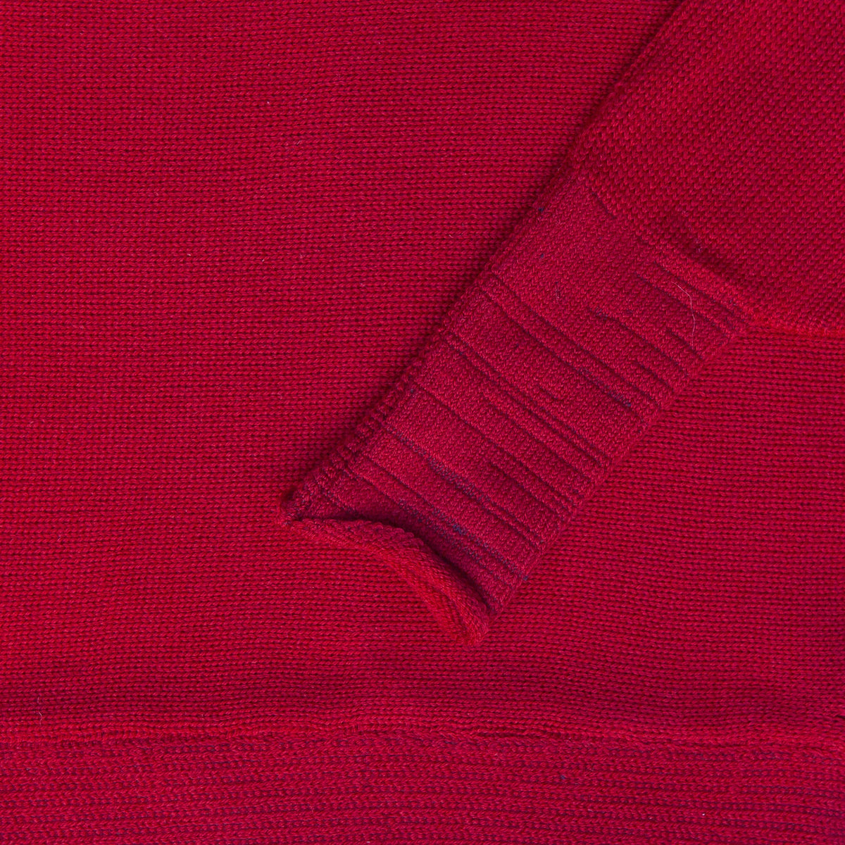 Detailansicht des Roteb gestrickten Pullover mit angeschnittenen Ärmeln. Man sieht das Ärmelbündchen.