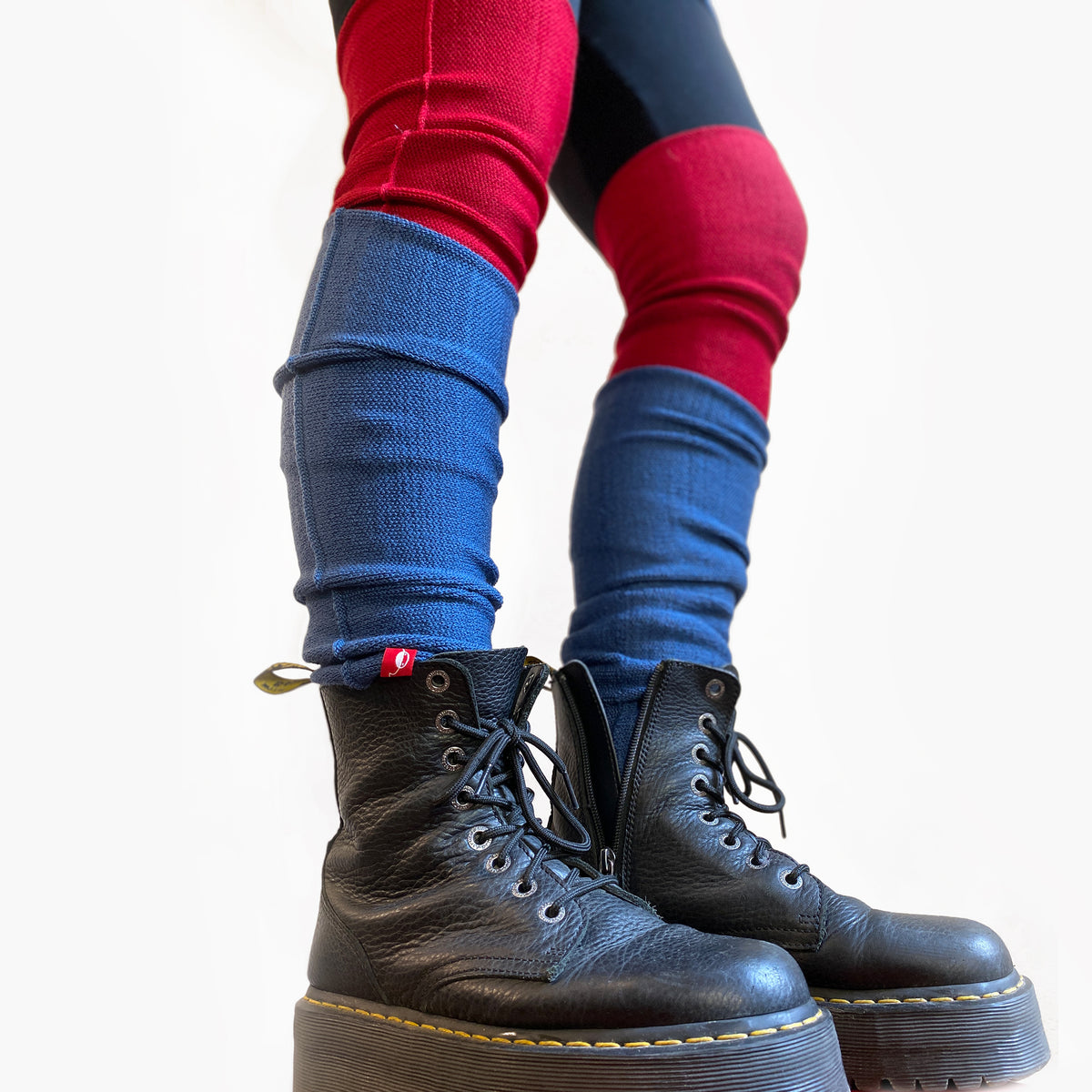 Man sieht ein paar Beine bis zum Knie. Sie tragen rote Beinstulpen bis übers Knie gezogen. Von vincente aus Wolle und darüber blauen Stulpen. Dazu trägt das Model DocMartens mit Plateaux
